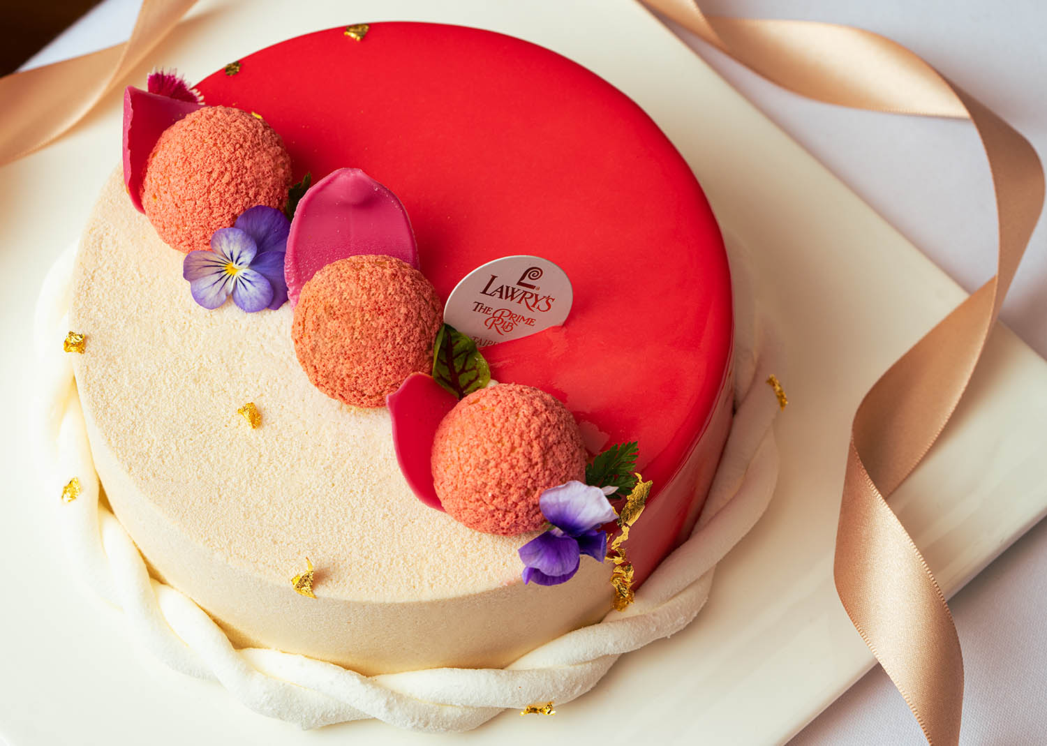 甜點主廚以同樣桃紅色系的伯爵巧克力香緹泡芙和藍紫色的食用花做搭配，並且綴以金箔片來增添貴氣。六吋售價NT$1,280。(圖片提供/Lawry's 勞瑞斯牛肋排餐廳)