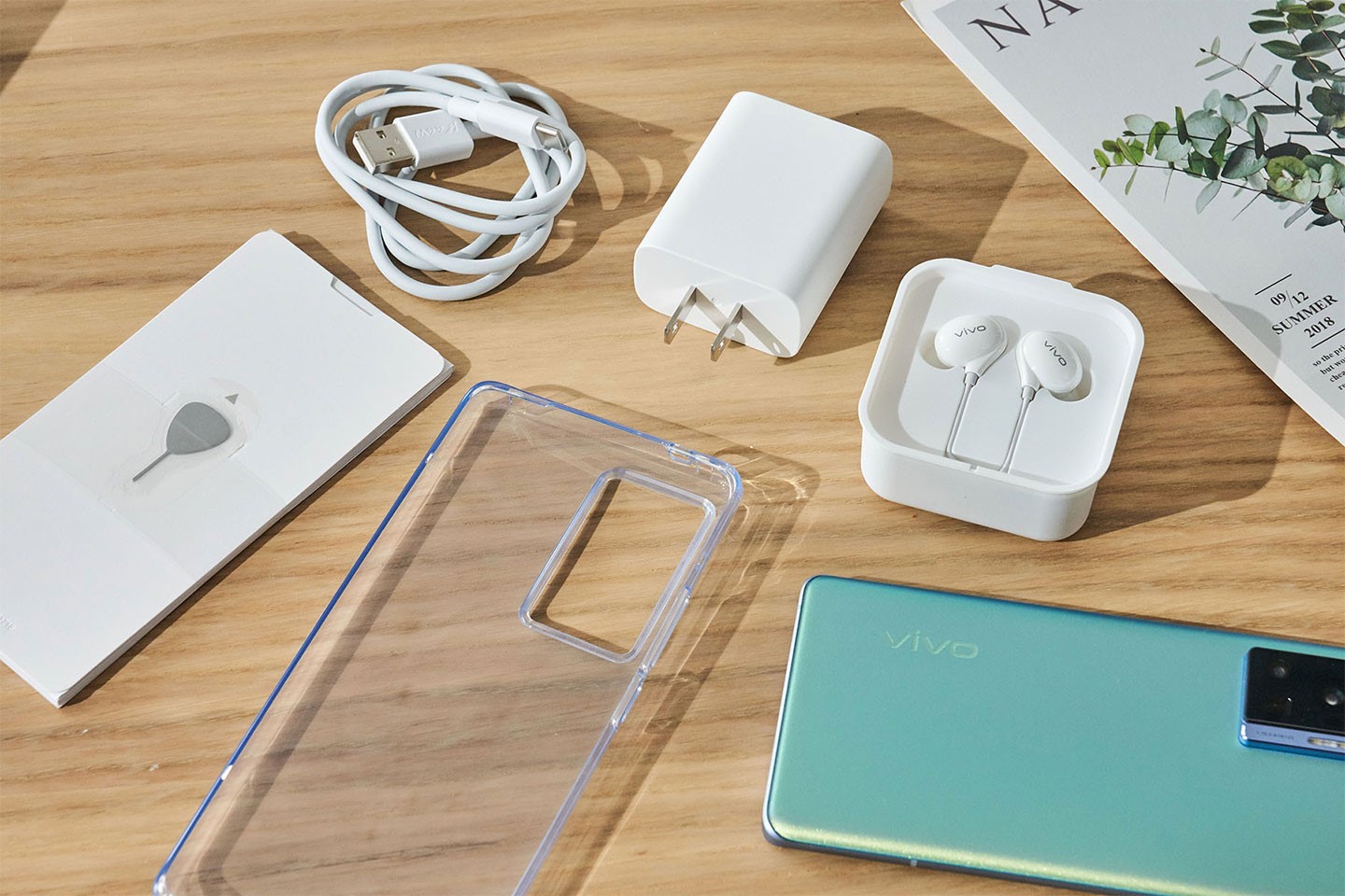 盒內所有物品一覽，除了手機本體與說明書之外，隨附的配件相當豐富，包括透明的清水保護套、充電線、充電器、有線耳機與退卡針。