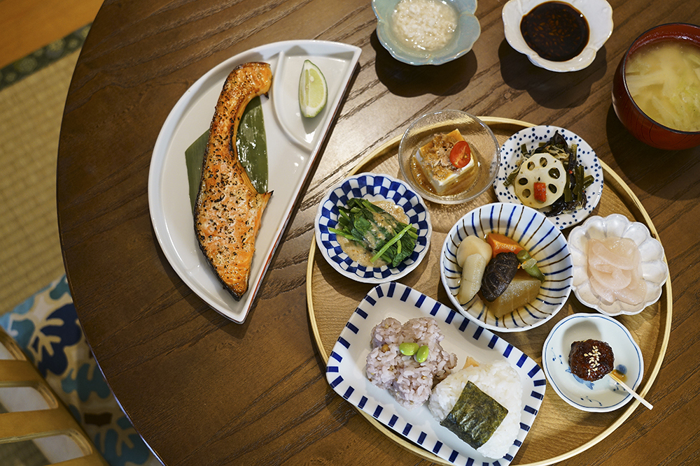 「有機鹽麴香烤鮭魚定食」──除了鮮香鹹甘、風味飽滿的烤鮭魚主菜，還有冷盤豆腐、胡麻醬菠菜、醬烤雞肉丸子、櫻花漬蘿蔔、燉蔬菜等隨著季節變換的配菜，豐盛如一幅色彩繽紛的畫作。(攝影/Cindy Lee)