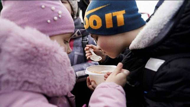 Children share bowls of soup after they and their mother leave Ukraine