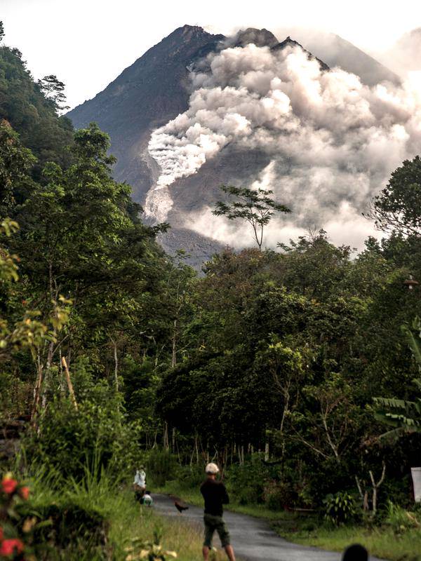 Orang-orang melihat Gunung Merapi yang memuntahkan batu dan abu di Yogyakarta (27/1/2021).  Potensi bahaya saat ini berupa guguran lava dan awan panas pada sektor selatan-barat daya meliputi sungai Boyong, Bedog, Krasak, Bebeng, dan Putih sejauh maksimal 5 kilometer.  (AFP/ Agung Supriyanto)