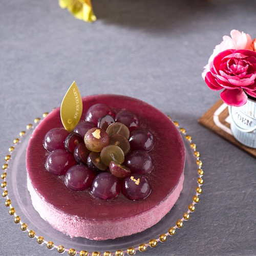 來自大村巨峰葡萄的春暖氣息~被譽為「葡萄之王」的巨峰葡萄色澤黝黑迷人，果汁濃厚甜美。「巨峰‧王漾」嚴選葡萄汁製成果凍，如紫紅晚霞泛著點點繁星。內層幼滑的綜合莓果慕絲配以濃厚朱古力蛋糕，口感細膩。底層夾