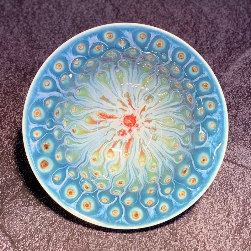 此作品是透過四到五層不同的釉藥層層堆疊，藉由每層施釉厚薄拿捏，並窯燒至1260度，歷經20小時的烈火淬煉，讓它在窯裡收縮流動，產生出孔雀羽毛的斑紋與流動感。