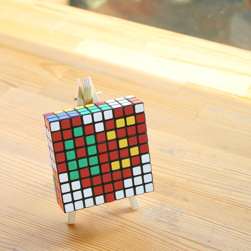 【商品概述】 設計師依照設計圖，將數個魔術方塊(Rubik's Cube)以純手工轉出正確的顏色組合後，拼湊固定成一幅馬賽克藝術般的文字或圖形，透過禮物盒包裝，製作出具有創意巧思又有特別意義的獨特禮物
