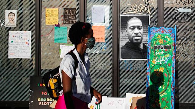 Seorang wanita melewati potret pria keturunan Afrika-Amerika, George Floyd yang dipasang saat penghormatan di sebuah halte yang dikelilingi buket bunga di Minneapolis, Minnesota, AS, 28 Mei 2020. Kematian Floyd yang mengundang kemarahan warga menimbulkan kerusuhan di Kota Minneapolis. REUTERS/Carlos Barria