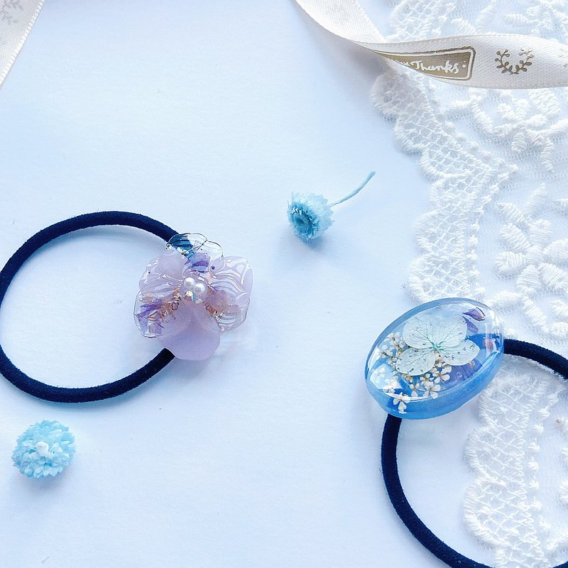 這兩個使用日本花材和模具製作的髮圈，使用了蕾絲花、毋忘我和繡球花做點綴，淡雅柔和的粉紫色花花最適合上班一族啦！清新甜美的冰藍色是爽朗系女孩必定要有的啊！簡約的設計不只個性十足，也方便在戴口罩的日子配戴，就算是束馬尾也可以很特別吧。