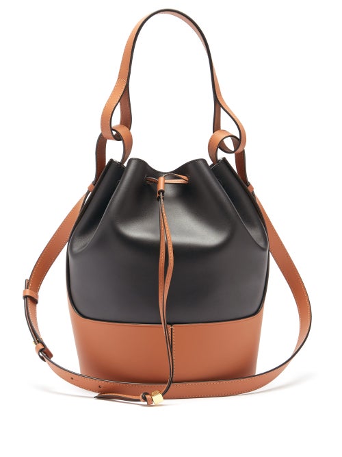 Loewe - Loewe's tan and black Balloon bag is named after the rounded silhouette which tapers to a gathered drawstring top. It's crafted in Spain from smooth leather debossed with the Anagram logo and rests on a structured base. The interlinked top handle and shoulder strap spotlight the label's affinity for experimental techniques.